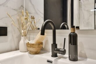 Modern fürdőszobai mosdó fekete csapteleppel, elegáns dekorációval és növényekkel.