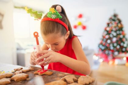 Egy kislány karácsonyi díszekkel a fején mézeskalácsot díszít.