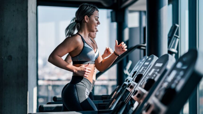 Egy fiatal nő fut a futópadon, energikus és motivált, modern edzőteremben.