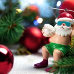 Egy vidám télapó figura, napszemüvegben és fürdőnadrágban, ünnepi díszek között.