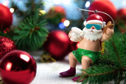 Egy vidám télapó figura, napszemüvegben és fürdőnadrágban, ünnepi díszek között.
