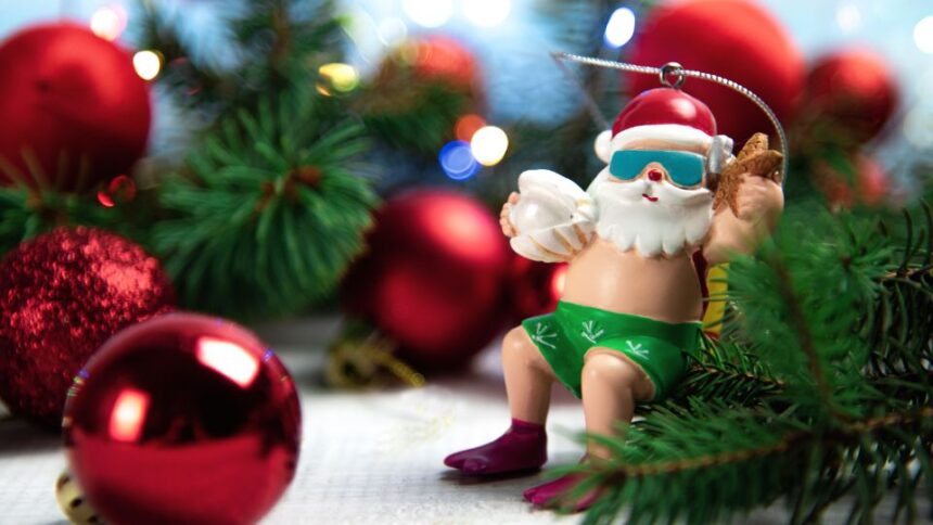 Egy vidám télapó figura, napszemüvegben és fürdőnadrágban, ünnepi díszek között.