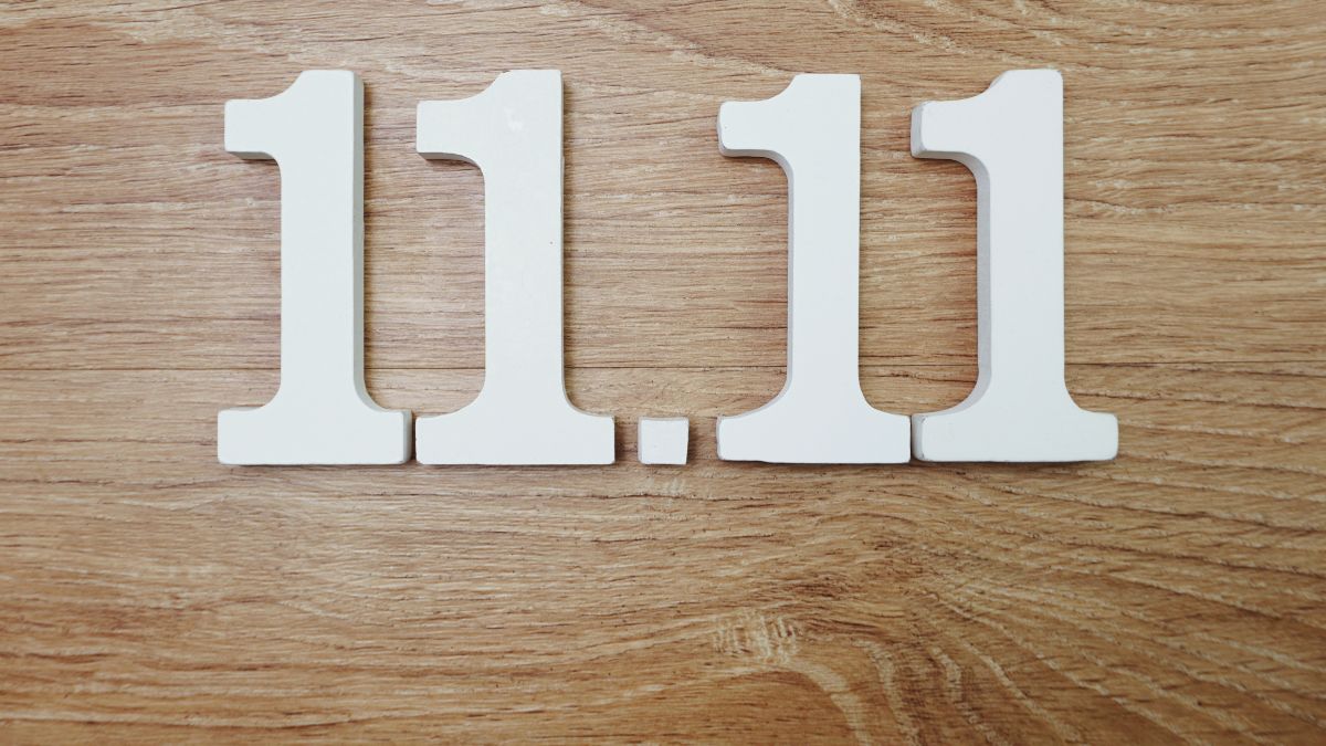 A képen a 11.11 számjegyek láthatók, fehér színben, fából készült háttéren.