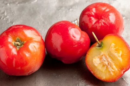 Friss, piros acerola gyümölcsök, köztük egy félbevágott darab, amely bemutatja a gyümölcs belsejét.