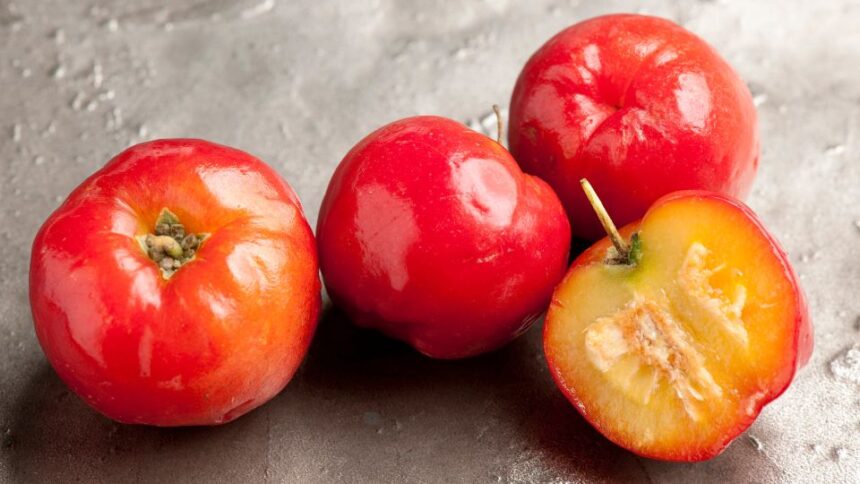 Friss, piros acerola gyümölcsök, köztük egy félbevágott darab, amely bemutatja a gyümölcs belsejét.