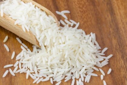 Friss, hosszú szemű basmati rizs egy fakanálból kiömlik, fa felületen.