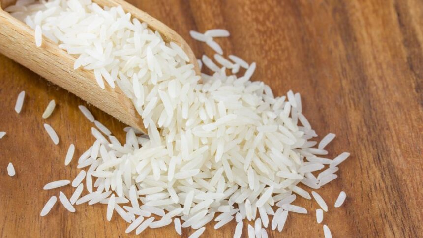 Friss, hosszú szemű basmati rizs egy fakanálból kiömlik, fa felületen.