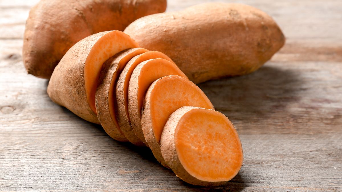 Szeletelt édesburgonya, mellette egy egész példány, fából készült asztalon.