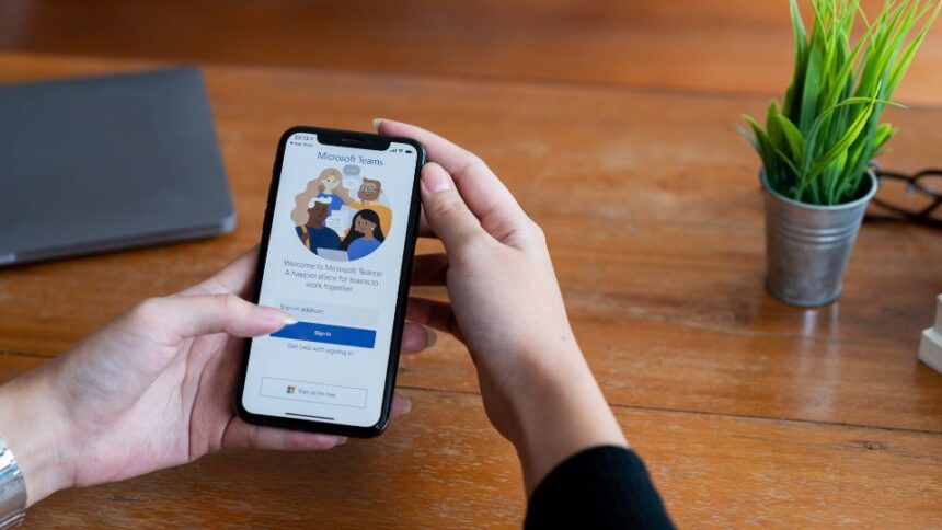 Egy kéz tart egy okostelefont, amelyen a Microsoft Teams bejelentkezési képernyője látható.