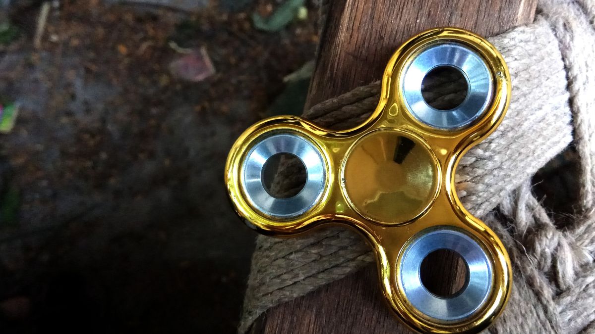 Egy arany színű fidget spinner, amely egy fa felületre van helyezve.