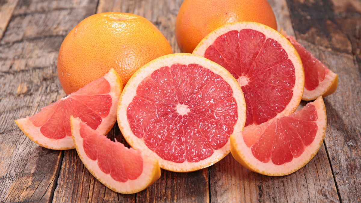 Friss grapefruitok és szeleteik, élénk színű húsukkal, fából készült háttér előtt.