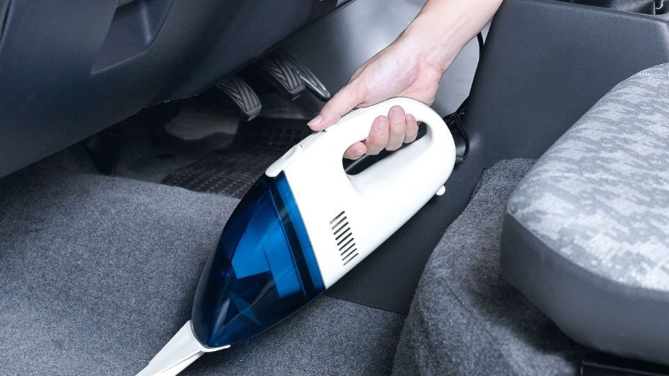 Kézi porszívó használata az autó belsejében, a padlón lévő szennyeződések eltávolítására.