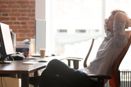 Egy férfi kényelmesen pihen az irodai székében, háttal a monitoroknak.