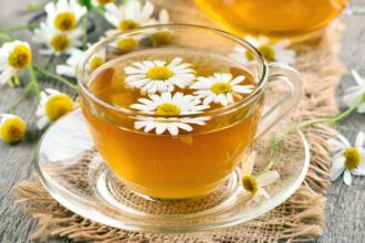 Egy átlátszó pohárban kamilla tea, virágokkal díszítve, fából készült asztalon.