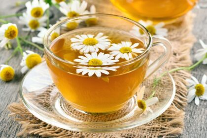 Egy átlátszó pohárban kamilla tea, virágokkal díszítve, fából készült asztalon.