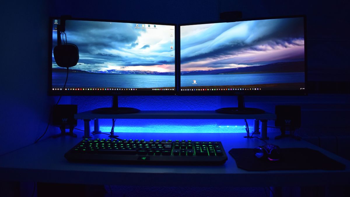Két LCD monitor egy asztalon, zöld háttérvilágítással és gamer billentyűzettel.