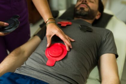 Egy férfi fekvő helyzetben, mágnesterápiás tapaszokkal a hasán, miközben egy szakember készíti elő a kezelést.