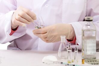 Egy laboratóriumi szakember gyógyszerek előkészítésével foglalkozik, üvegek és fecskendők között.