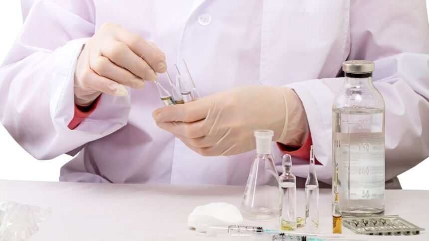 Egy laboratóriumi szakember gyógyszerek előkészítésével foglalkozik, üvegek és fecskendők között.