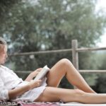 Egy fiatal lány relaxál a szabadban, könyvet olvasva egy napernyő alatt.