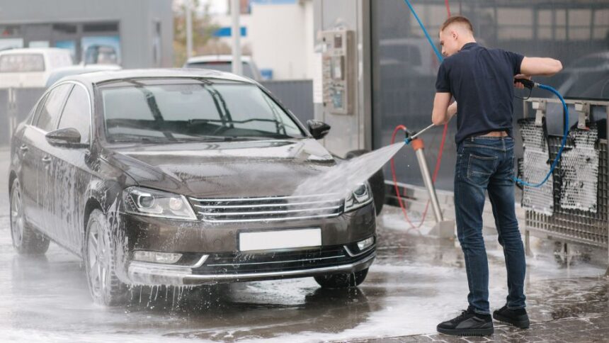 Egy fiatal férfi önkiszolgáló autómosóban mossa le a fekete autóját.