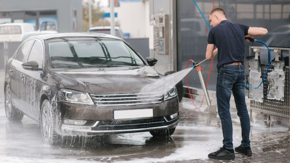 Egy fiatal férfi önkiszolgáló autómosóban mossa le a fekete autóját.
