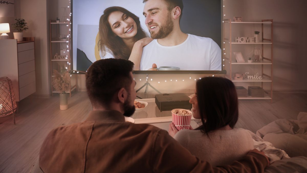 Egy pár együtt nézi a tévét, miközben popcornnal és italokkal pihen.