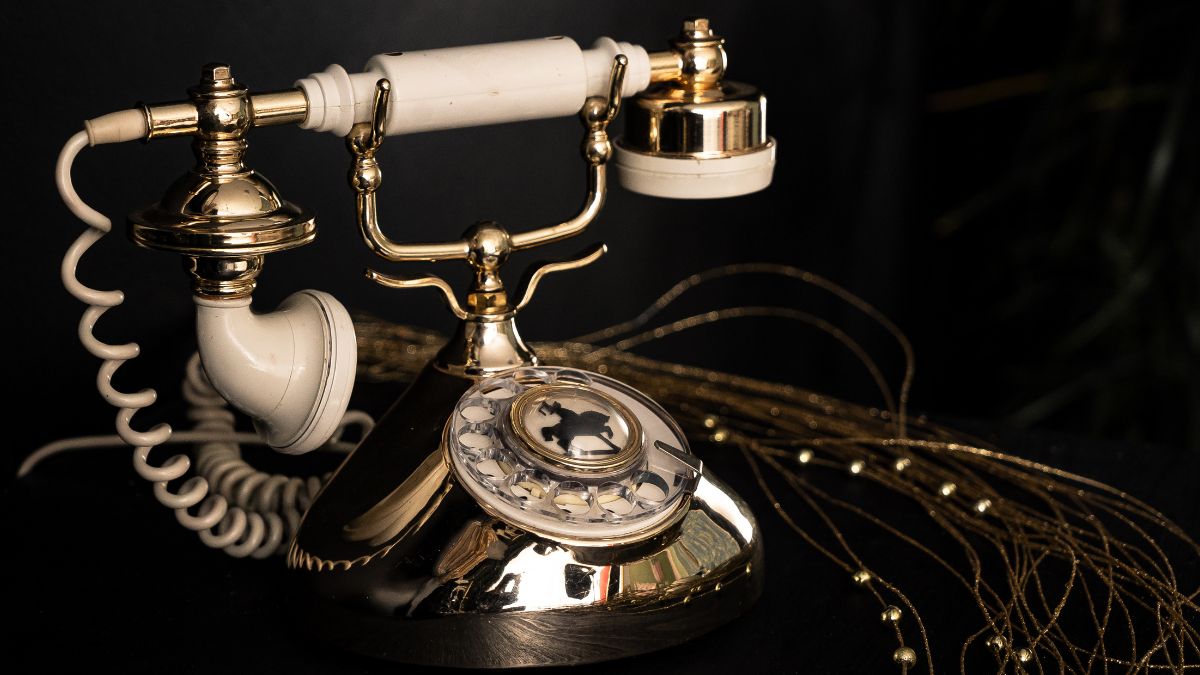 Egy elegáns tárcsás telefon, aranyozott részletekkel és fehér fülhallgatóval, retro stílusban.