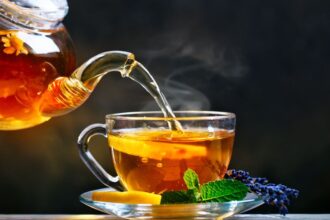 Gőzölgő tea citromszeletekkel és friss mentával egy üvegcsészében.