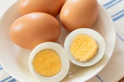 Két főtt tojás és három nyers tojás egy fehér tányéron, friss és tápláló megjelenésben.