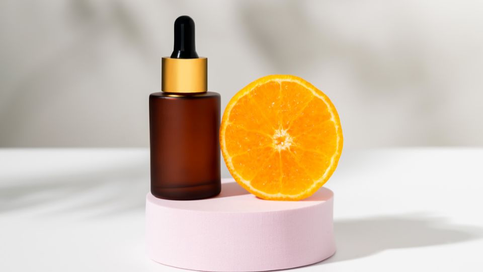 E-vitaminos szérum üveg és félbevágott narancs egy rózsaszín alapon.