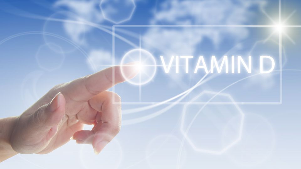 Egy kéz érintése a levegőben, amelyen a 'VITAMIN D' felirat látható, világos háttérrel.