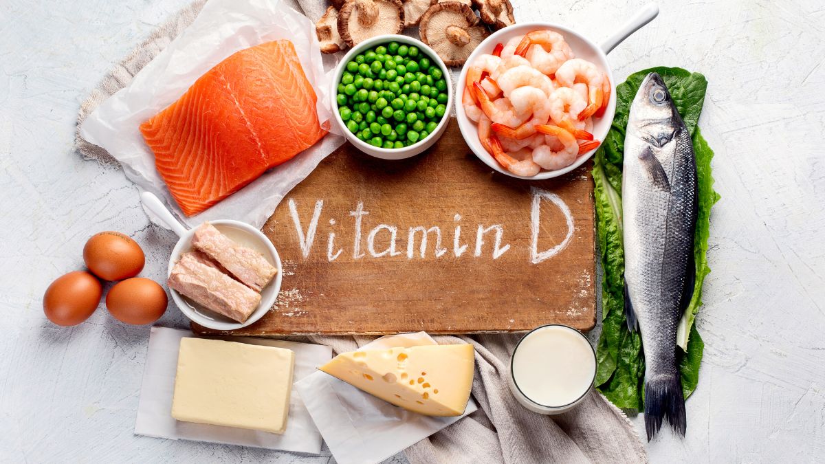 D-vitamint tartalmazó ételek, mint a lazac, tojás, tej és zöldborsó egy fából készült deszkán.