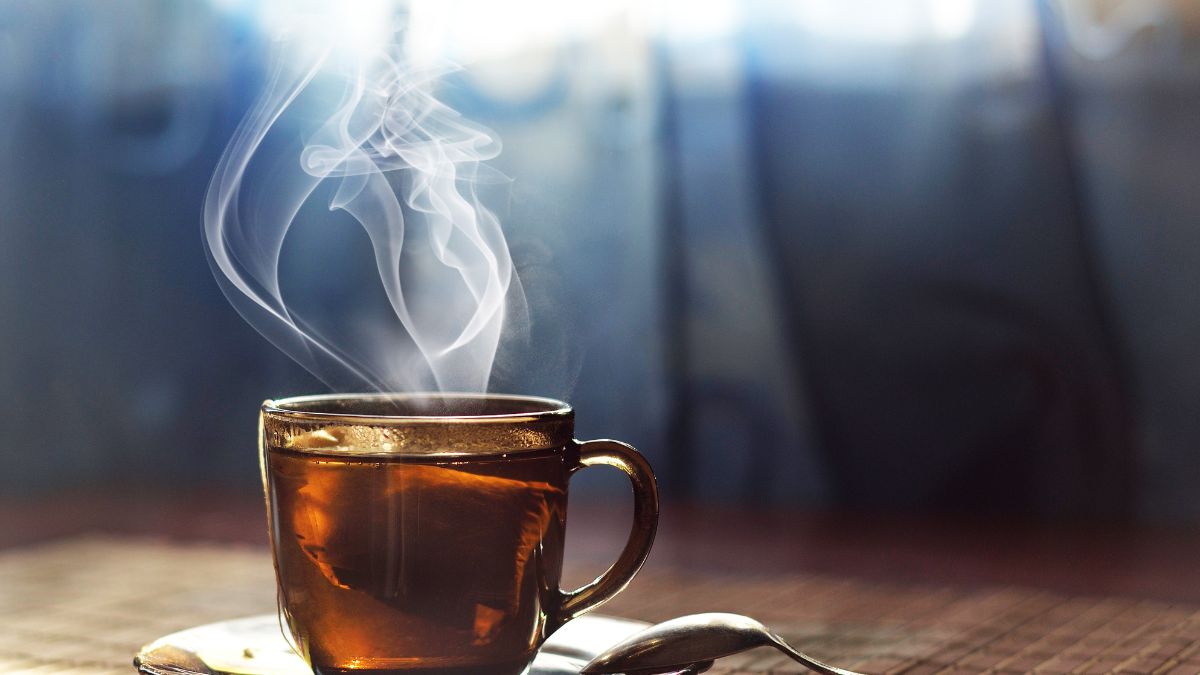 Gőzölgő fekete tea egy átlátszó bögrében, háttérben lágy fényekkel.
