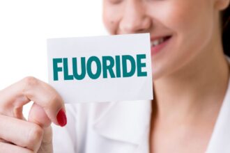 Egy nő mosolyogva tart egy papírlapot, amelyen a 'FLUORIDE' felirat olvasható.