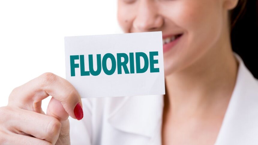 Egy nő mosolyogva tart egy papírlapot, amelyen a 'FLUORIDE' felirat olvasható.
