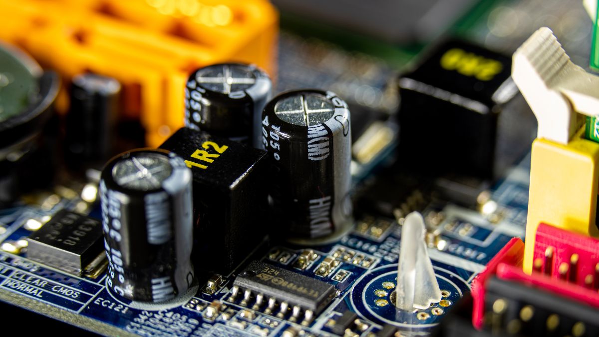 Közeli kép kondenzátorokról és egyéb elektronikai alkatrészekről egy áramkörön.