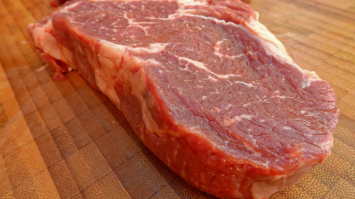 Egy friss marhahús szelet, amely a vágódeszkán fekszik, jól látható zsíros részekkel.