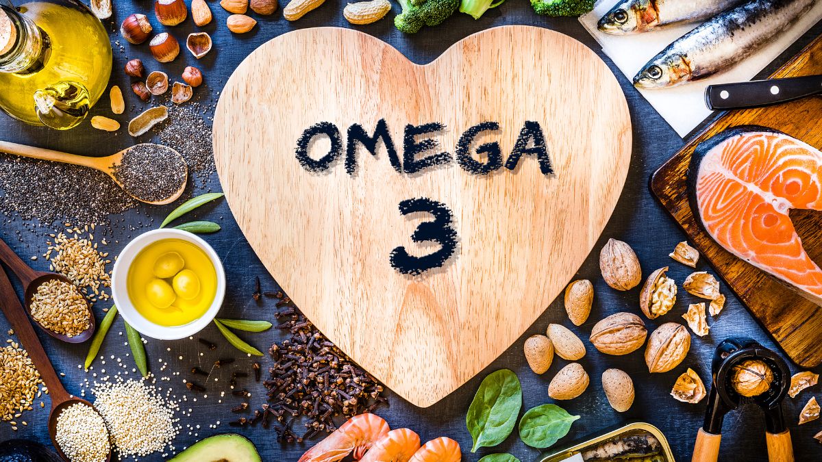 Egy szív alakú vágódeszkán az 'OMEGA 3' felirat látható, körülötte különböző omega-3 források, mint hal, magvak és olajok.