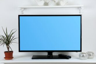 Egy plazma TV látható, kék háttérrel, mellette növény és dísztárgyak.