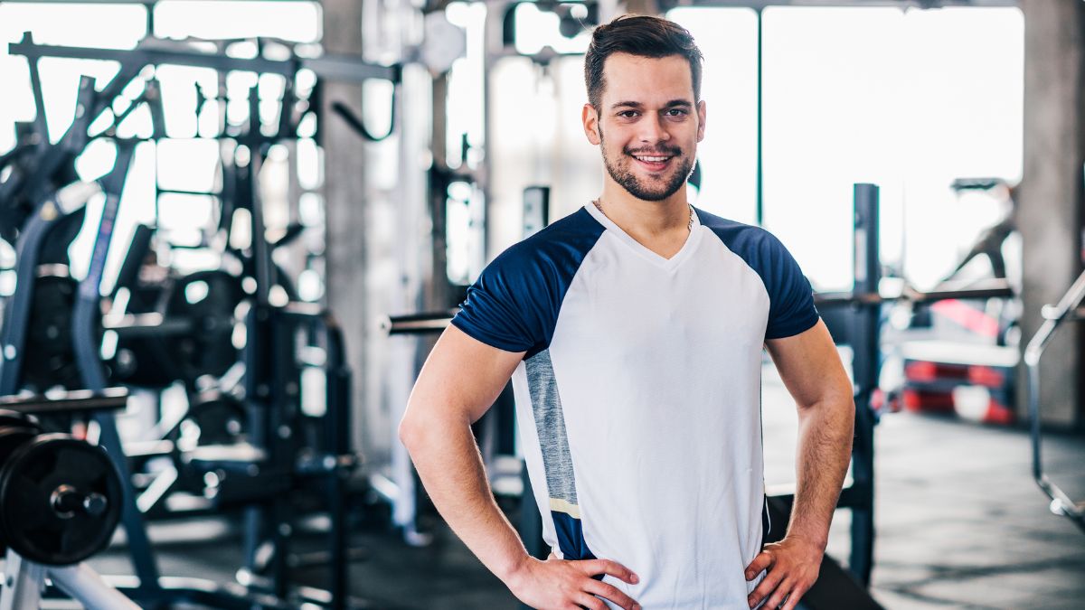 Egy fiatal férfi mosolyogva áll egy edzőteremben, sportos ruhában.