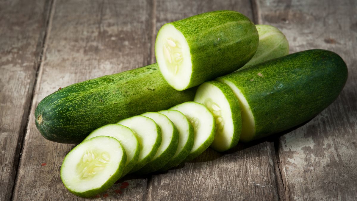 Friss uborkák és szeleteik egy fából készült felületen, tükrözve az egészséges táplálkozást.