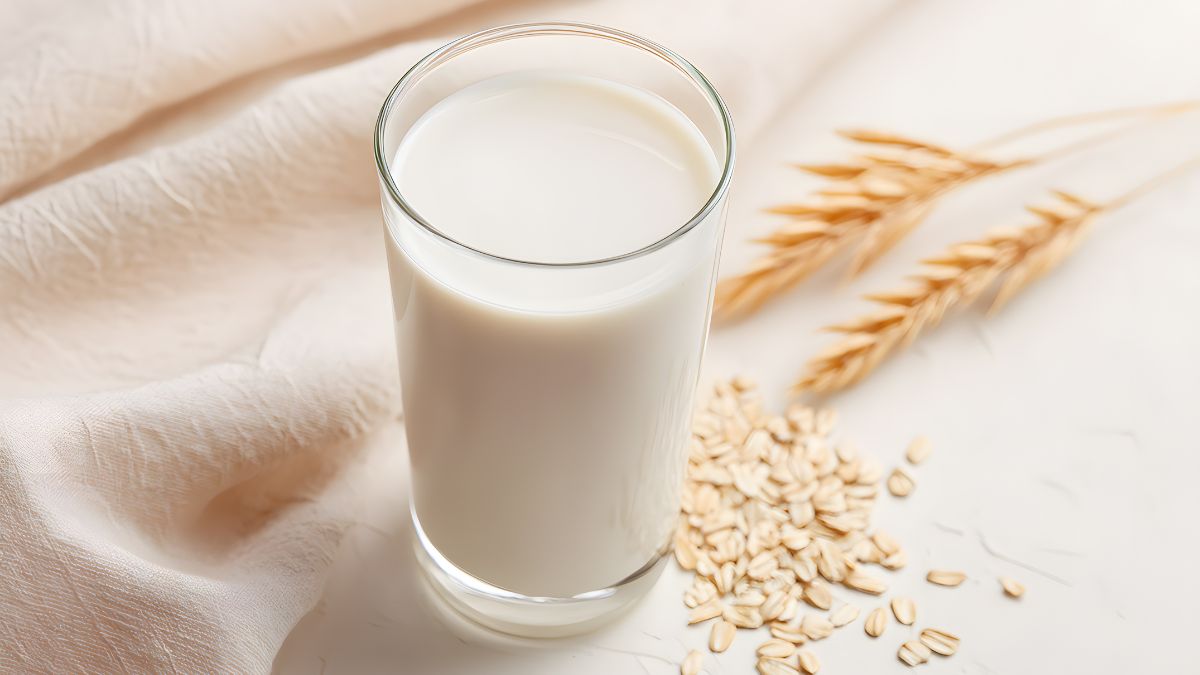 Egy pohár zabtej, mellette zabpehely és búzaszemek, egészséges alternatíva.