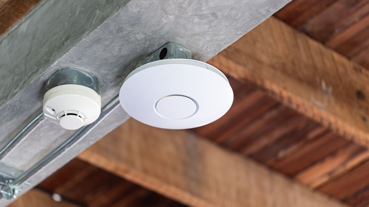 Egy fehér access point látható a mennyezeten, mellette egy füstérzékelő.