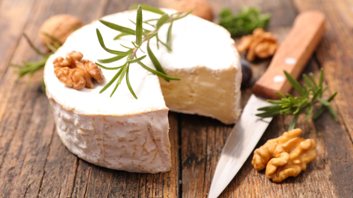 Friss Camembert sajt, dióval és rozmaringgal díszítve, fából készült deszkán.