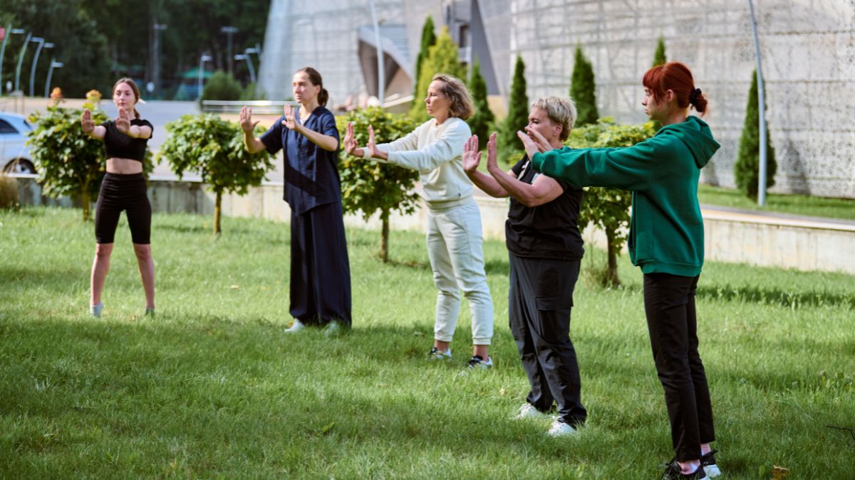 Öt ember gyakorol Chi Kungot egy zöld parkban, harmonikus mozdulatokkal.