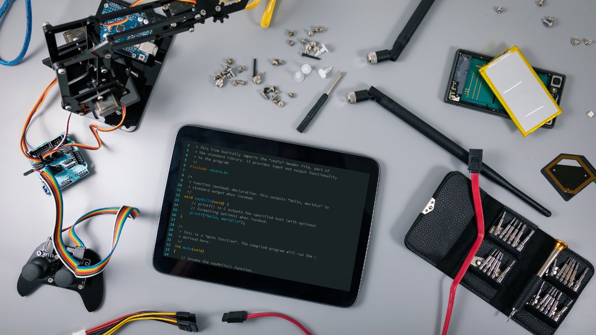 Egy elektronikai munkaasztal, ahol különböző alkatrészek és egy tablet látható programozási kóddal.
