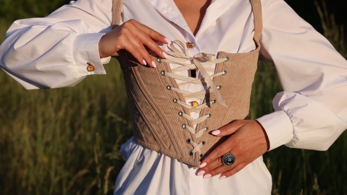 Egy nő fűzőt köt a fehér ingje fölött, a háttérben zöld fűvel.