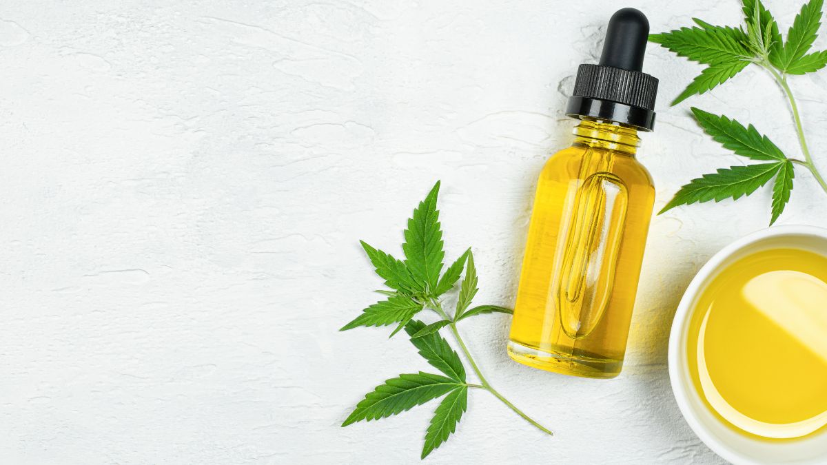 Egy üveg hasisolaj pipettával és friss kannabiszlevelek egy fehér háttéren.
