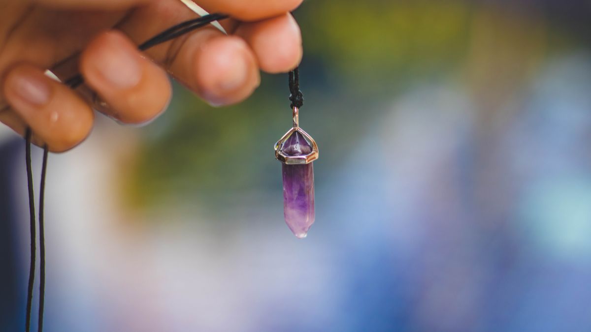 Egy hegyikristály nyaklánc lóg egy kézben, gyönyörű lila színben.